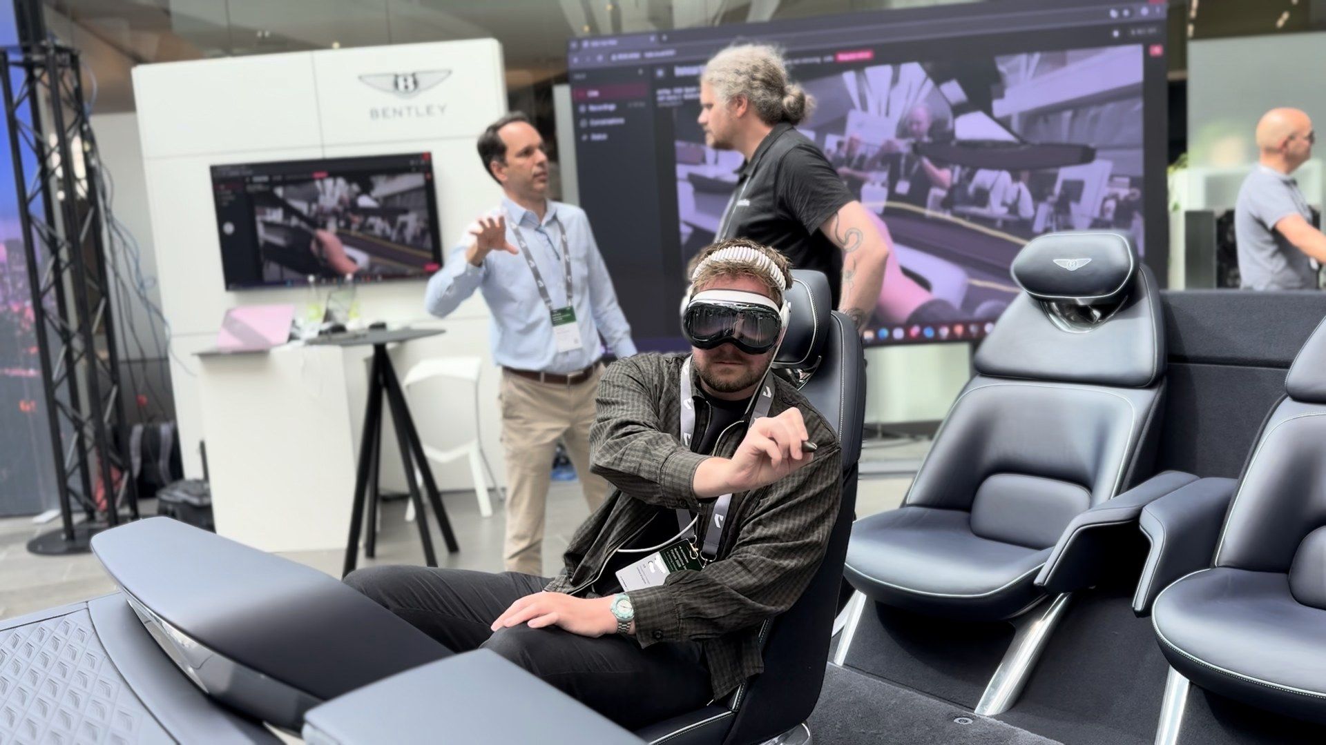 A reviewer wearing Apple Vision Pro seated in a physical Bentley seating buck, gesturing mid-air, with live Innoactive Spatial session screens behind them