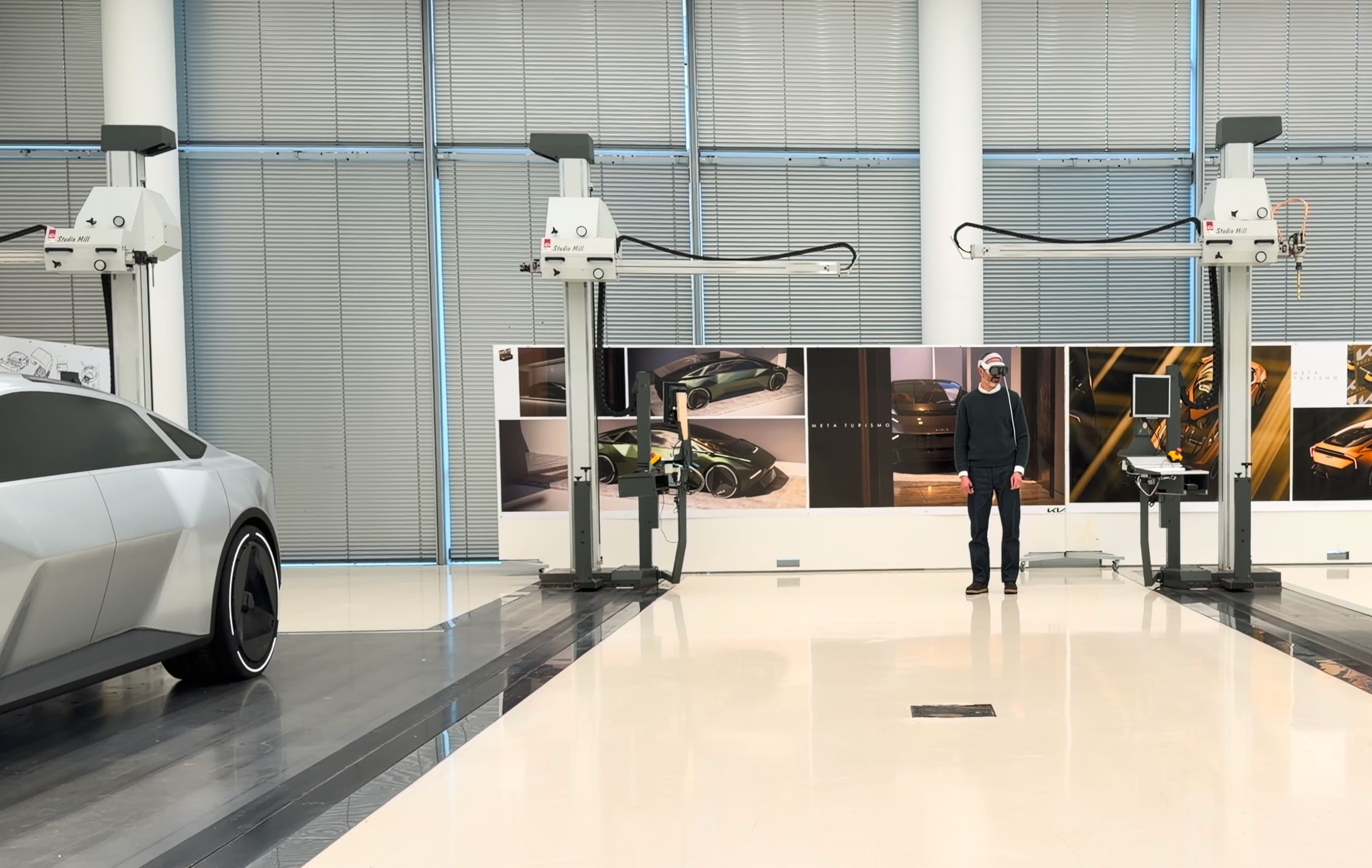 Designer wearing Apple Vision Pro standing in an automotive design studio between studio mills, with a silver Kia concept on the side and design sketches in the background.